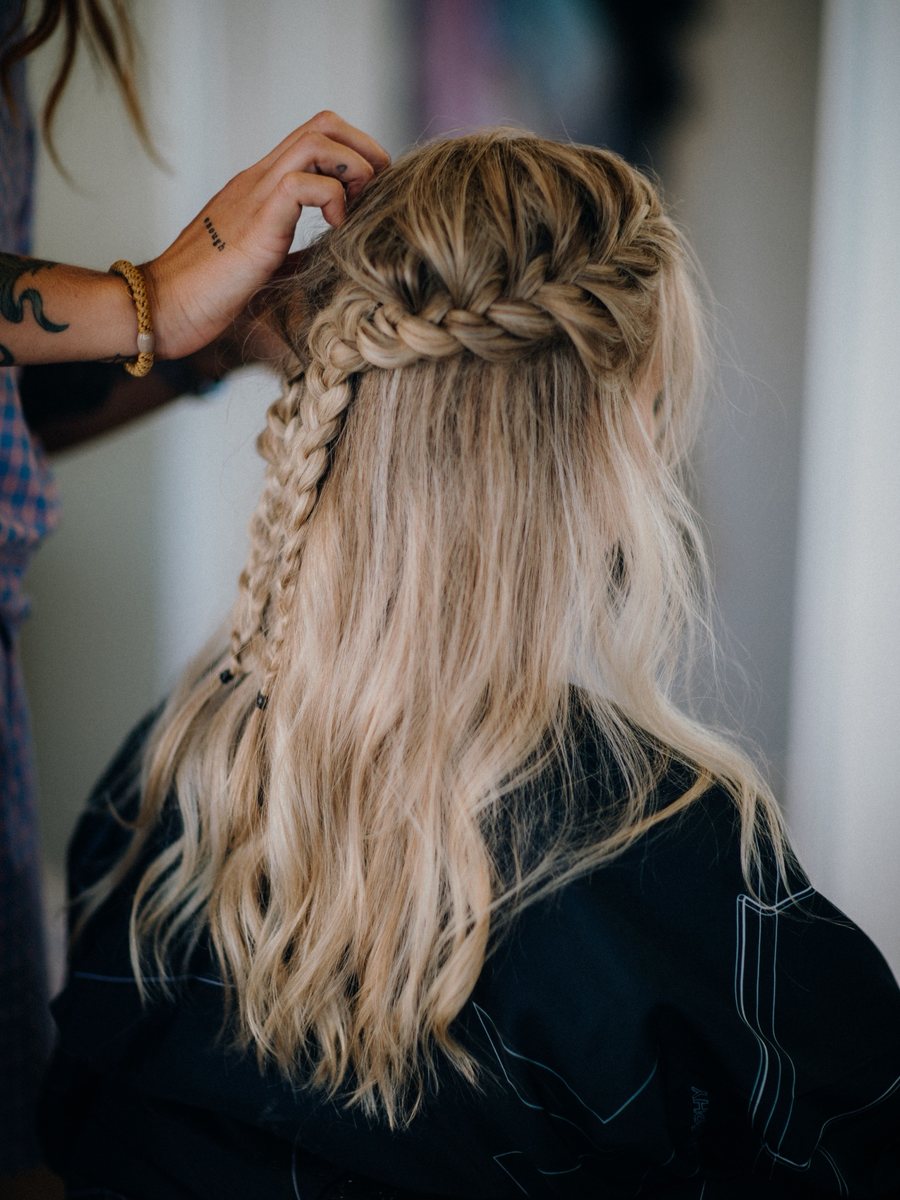 Stylist pinning a soft half-up braid into long blonde waves.