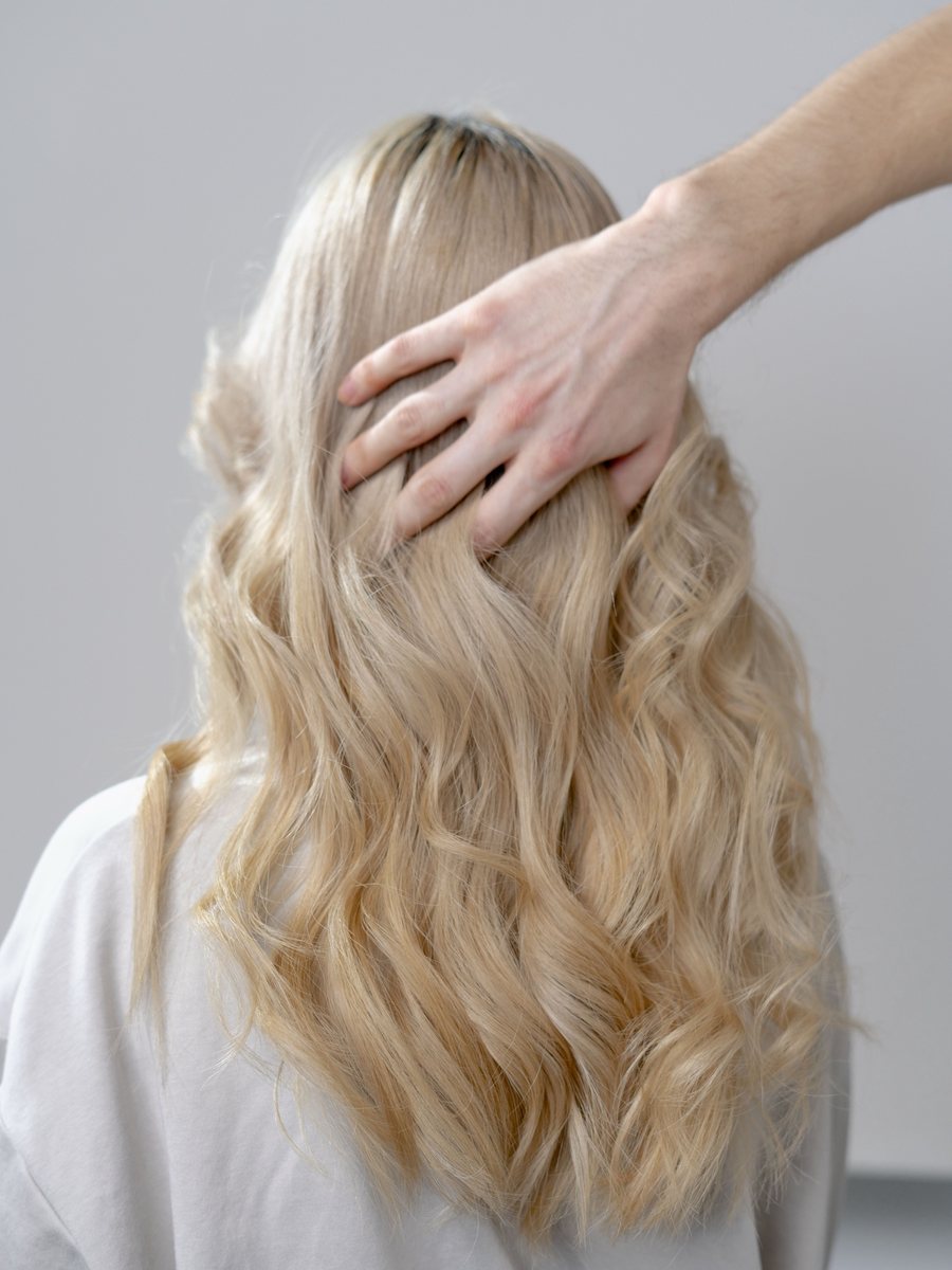 Long, soft blonde waves seen from behind, with a hand lifting the hair.