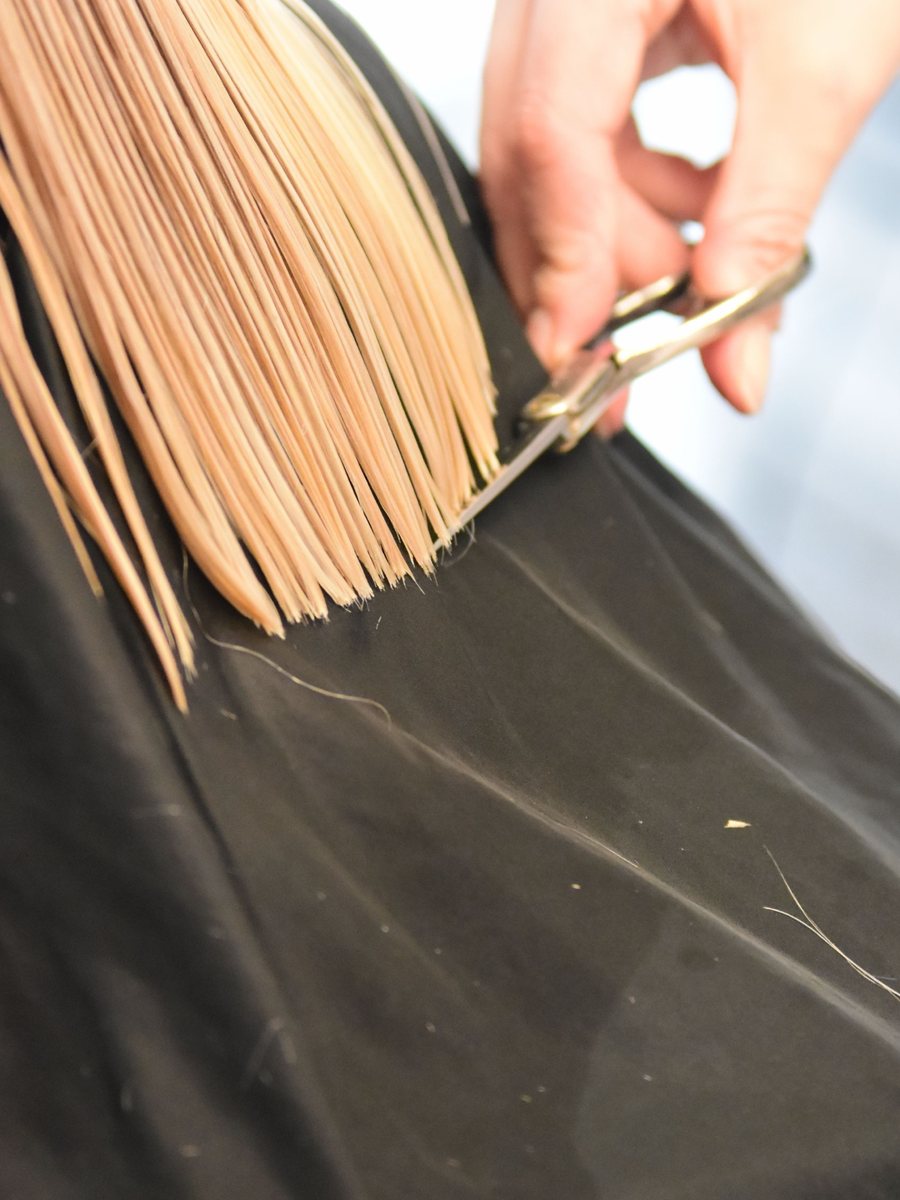 Stylist cutting a clean line through blonde hair over a black cape.