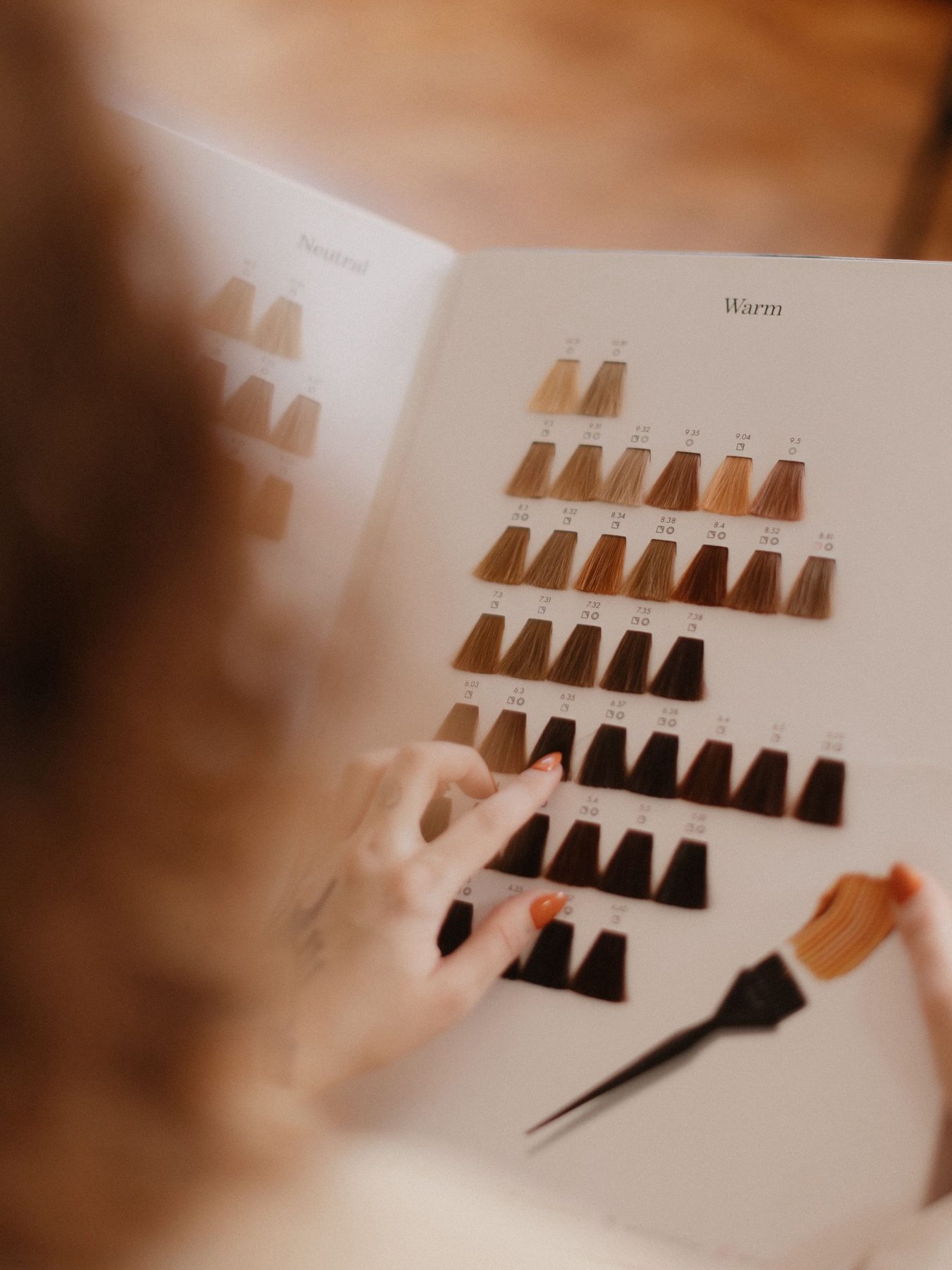 A stylist's hand choosing a shade in a hair color swatch book, with a tint brush.