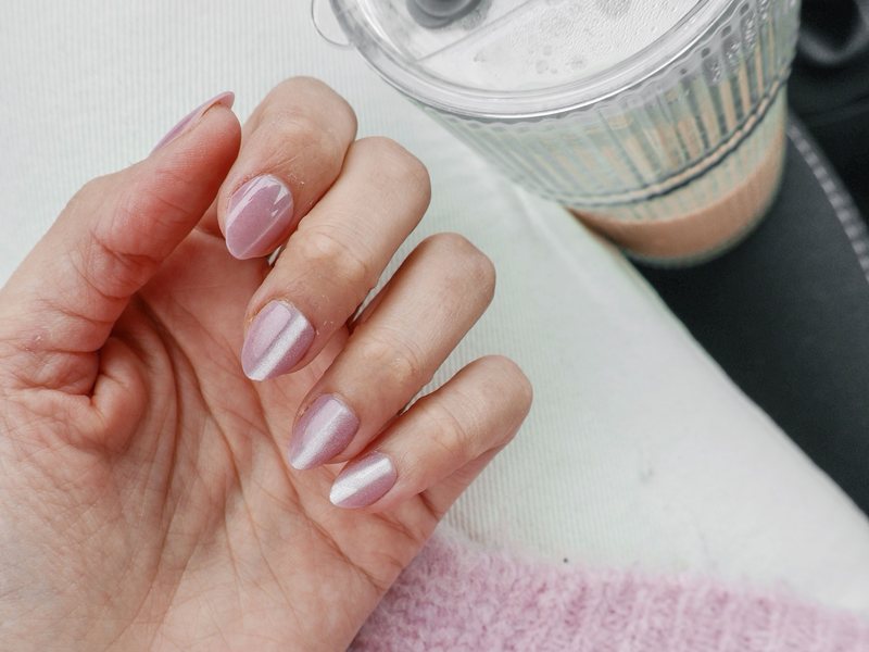 Short almond nails with a pink pearl chrome finish, next to a fluffy pink sweater.