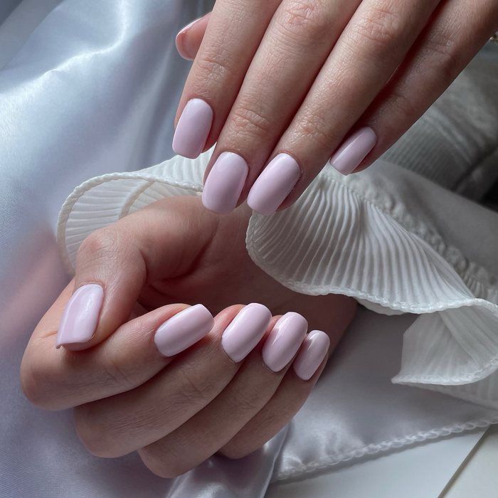 Milky pink square nails resting on white satin.