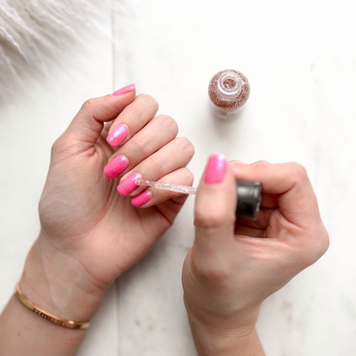 Hot pink glitter nails being finished with a sparkly top coat.