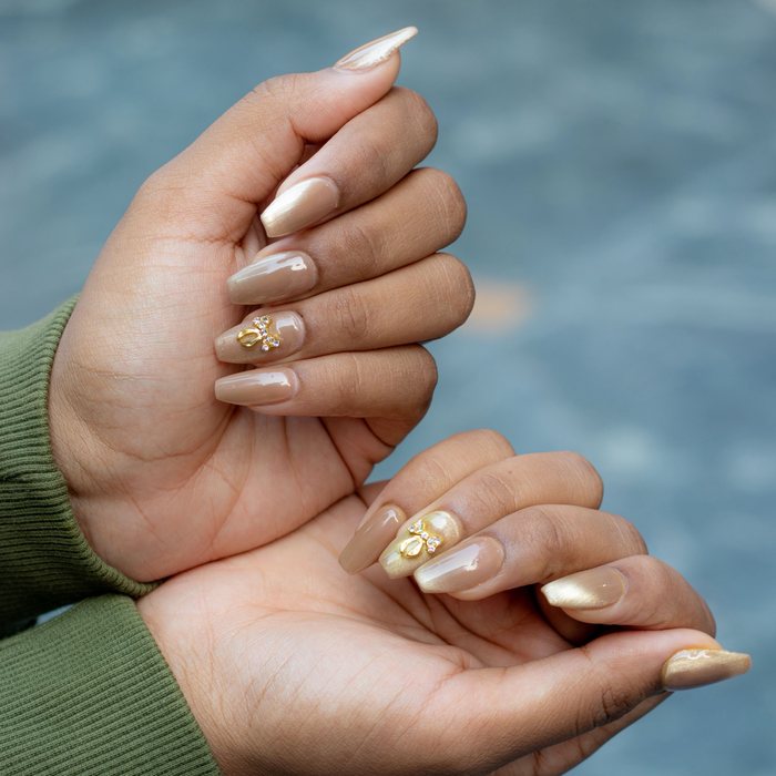 Nude coffin nails with a shimmer finish and a gold bow charm.