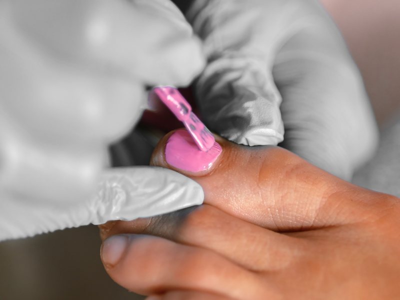 A nail tech in gloves painting a toenail bubblegum pink.